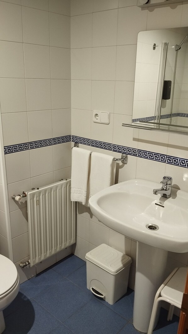A bathroom with a white sink, a toilet, a small trash bin, a towel rack, and a mirror. - Hotel Covaleda Soria (Covaleda)