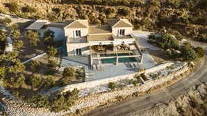 Vista aérea de una casa moderna con piscina, muros de piedra y un paisaje circundante.