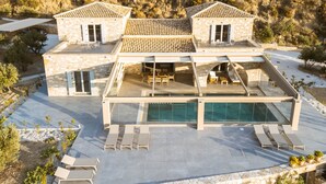Una villa moderna con piscina cubierta de vidrio, zona de estar exterior y arquitectura de piedra.