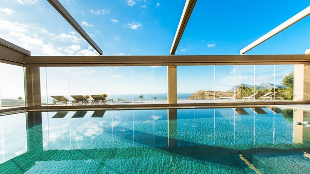 Una piscina infinita moderna con agua cristalina, sillas de descanso y vistas al océano y las montañas.