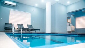 Una piscina interna moderna con acqua cristallina, due lettini prendisole e un'ampia finestra con tende.