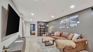 A modern living room with a sectional sofa, a coffee table, and a flat-screen TV mounted on the wall.