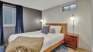 A modern bedroom with a wooden bed, a nightstand, a small desk, and a window with curtains.