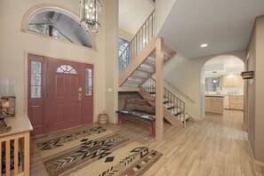 A spacious foyer with a wooden staircase, a red door, and a patterned rug.