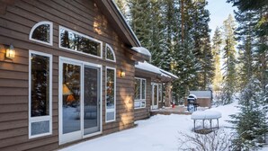 Una cabaña de madera con amplias ventanas, un espacio de estar cubierto al aire libre y un paisaje cubierto de nieve.