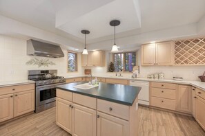 Een moderne keuken met een centraal eiland, roestvrijstalen apparatuur en licht houten kastjes.