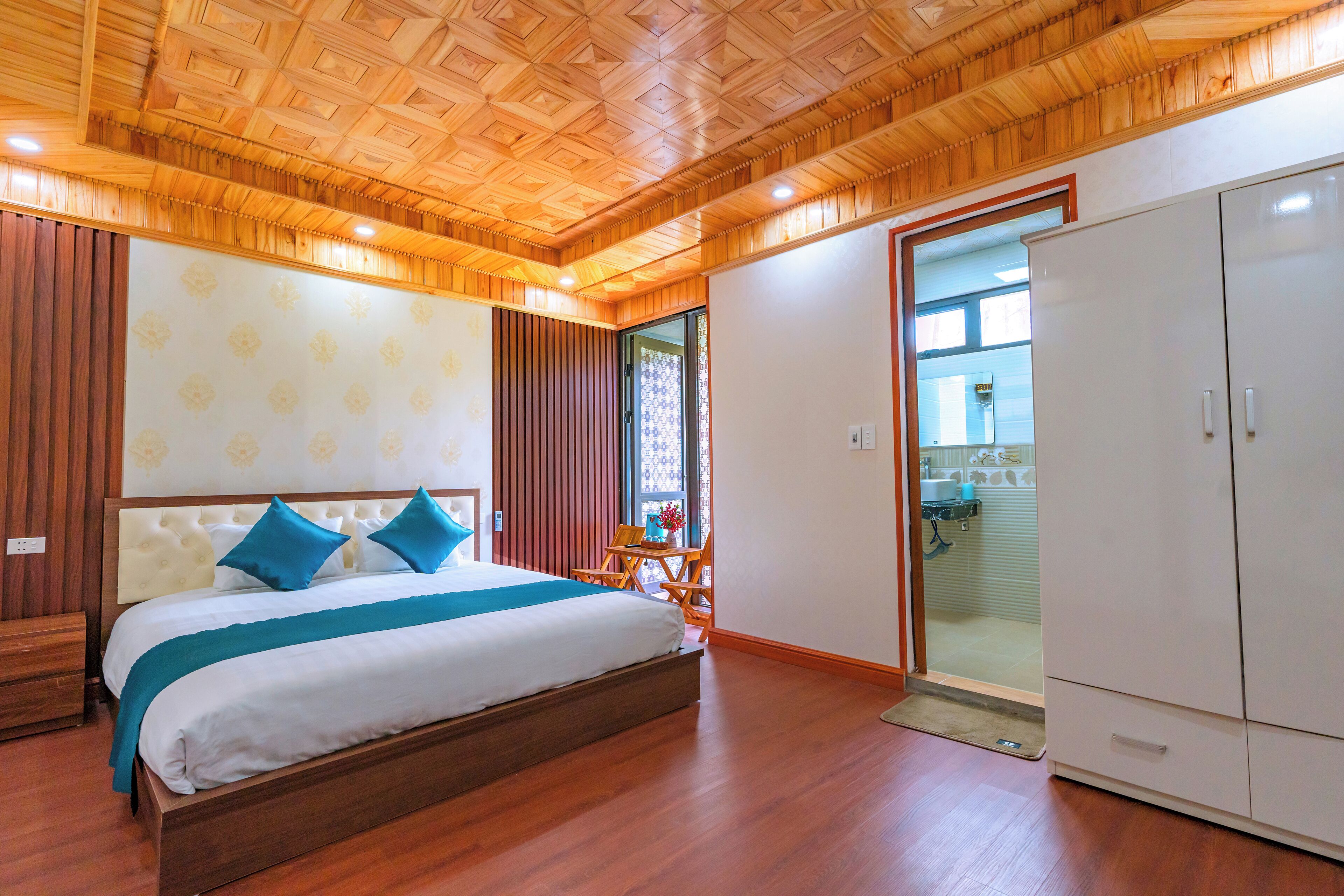 Une chambre avec un plafond en bois, un grand lit avec des oreillers bleus, une armoire et une vue sur la salle de bain.