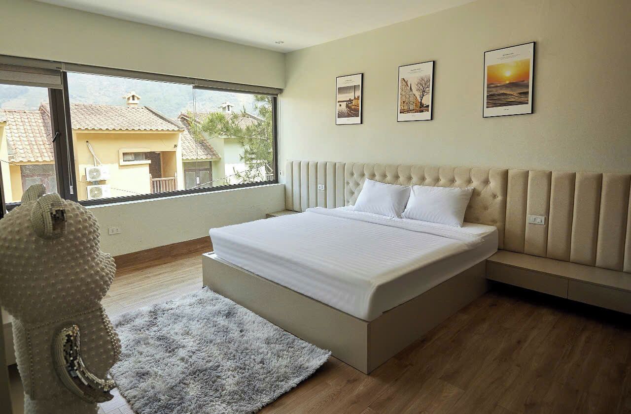A bedroom with a large bed, a view of the outside, and three framed pictures on the wall.