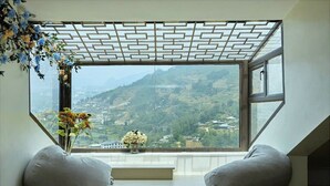 Une pièce dotée d’une grande fenêtre donnant sur un paysage montagneux, d’un plafond décoratif et d’un banc agrémenté de coussins.