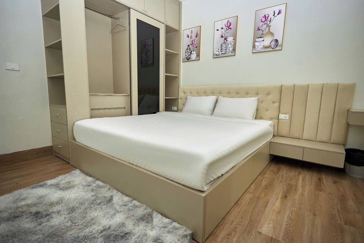Un dormitorio con una cama grande, un armario empotrado, un banco y obras de arte en la pared.