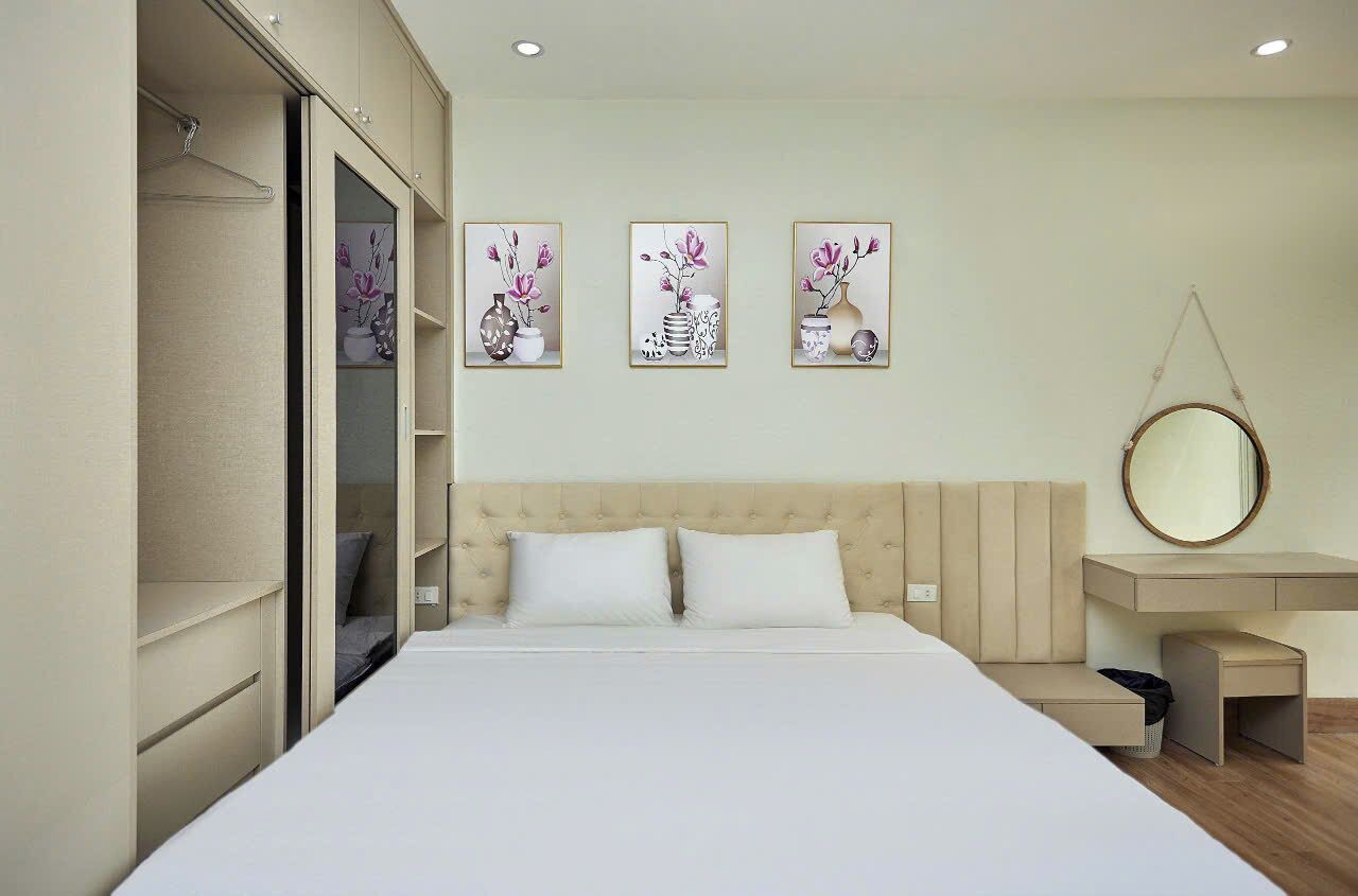 A bedroom with a bed, a bedside table, a hanging mirror, and three wall-mounted artworks.