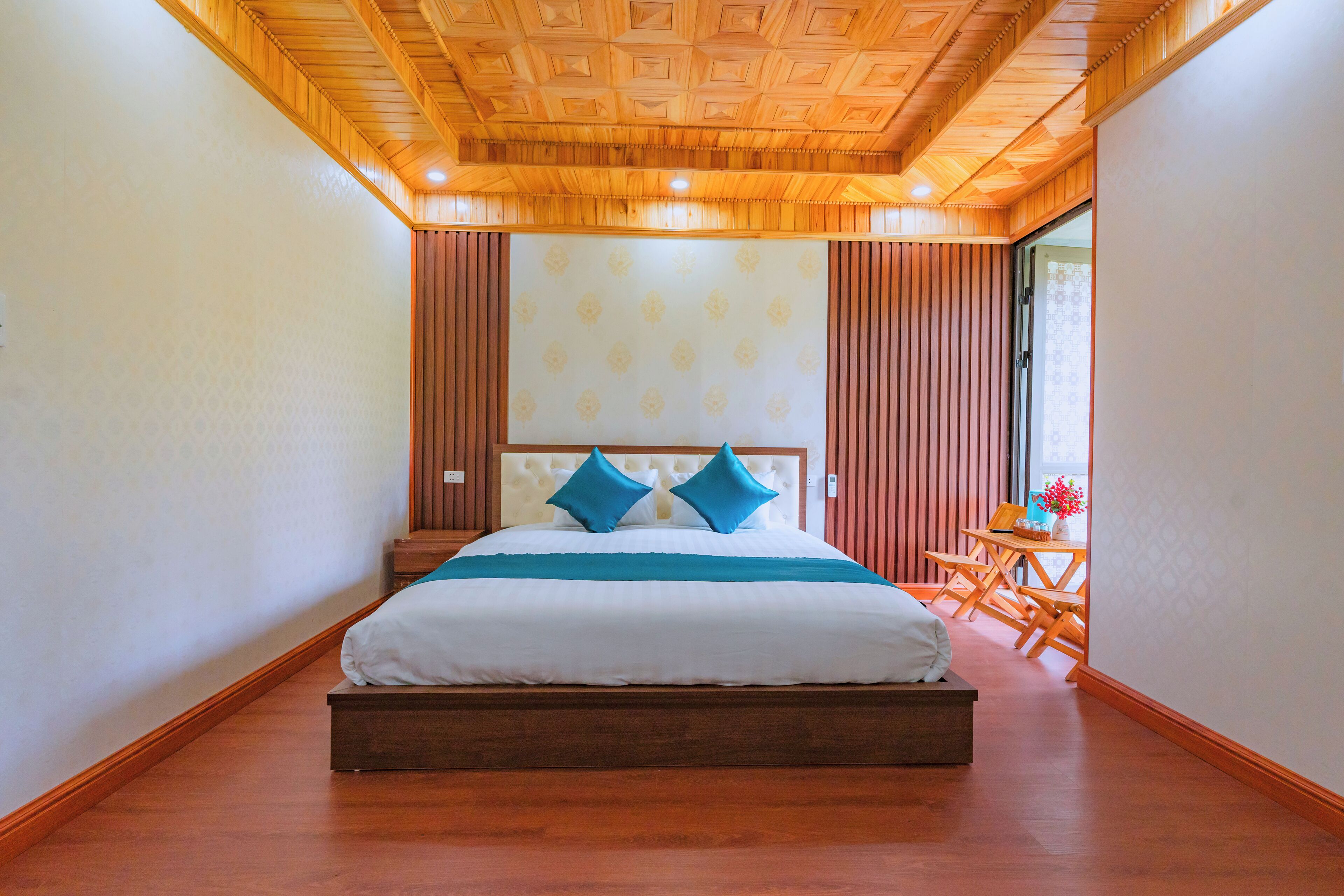 Ein Schlafzimmer mit Holzboden und -decke, einem Bett mit weißer Bettwäsche und blauen Kissen sowie einem Fenster mit Blick ins Freie.