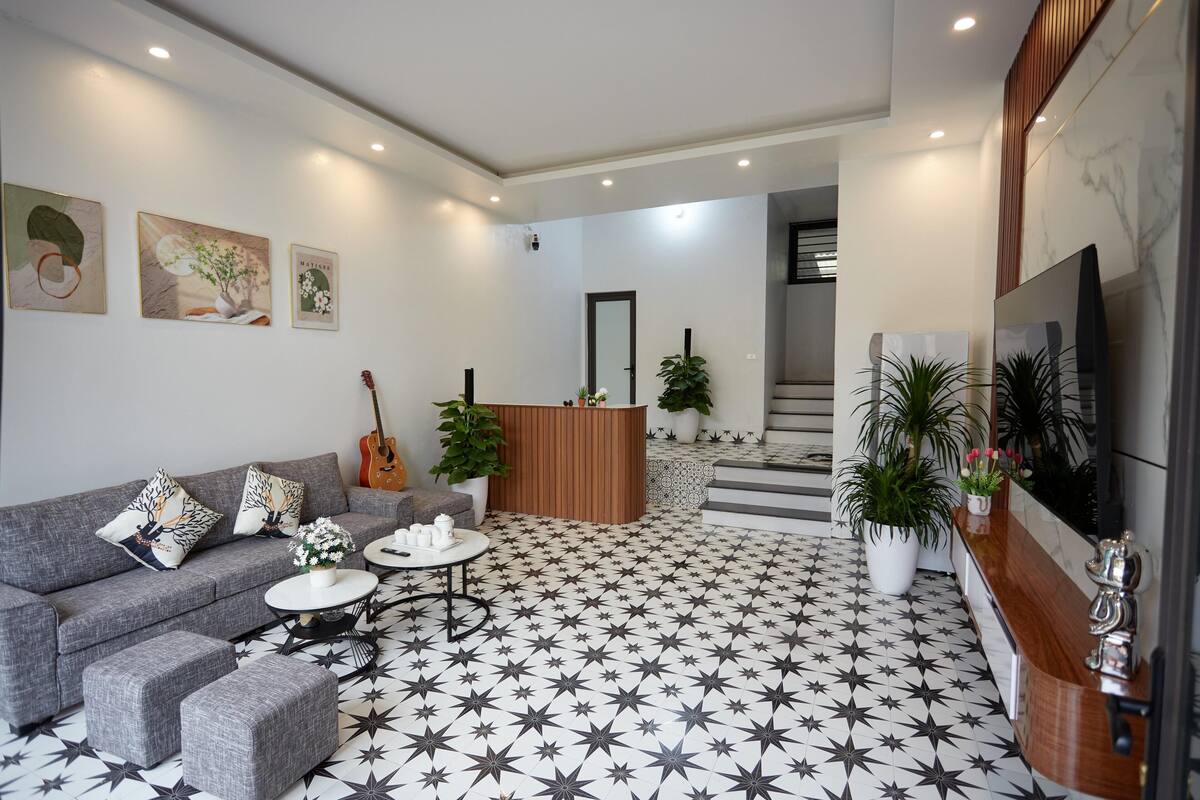 Una sala de estar moderna con un sofá gris, una mesa de centro y un suelo estampado. Se observa una recepción con un panel de madera y un televisor montado en la pared.