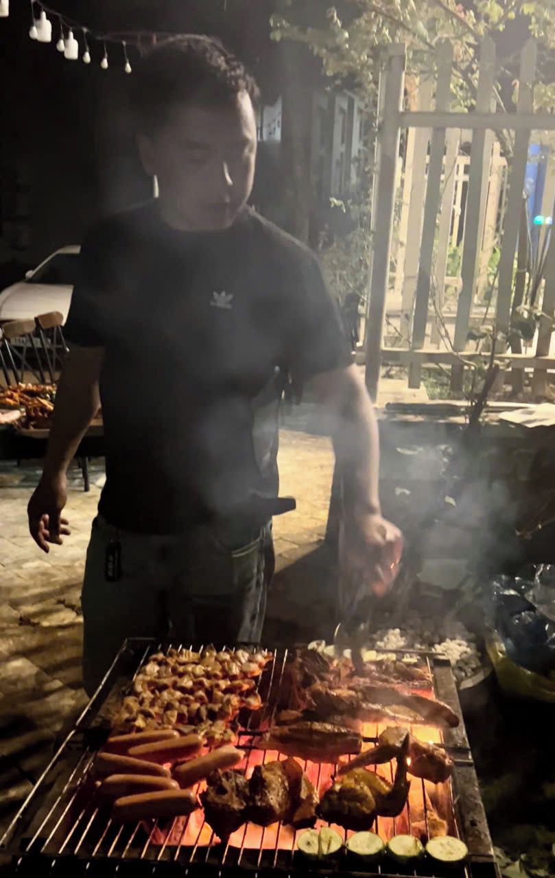 Henkilö grillaa erilaisia lihoja ja vihanneksia ulkona yöllä.