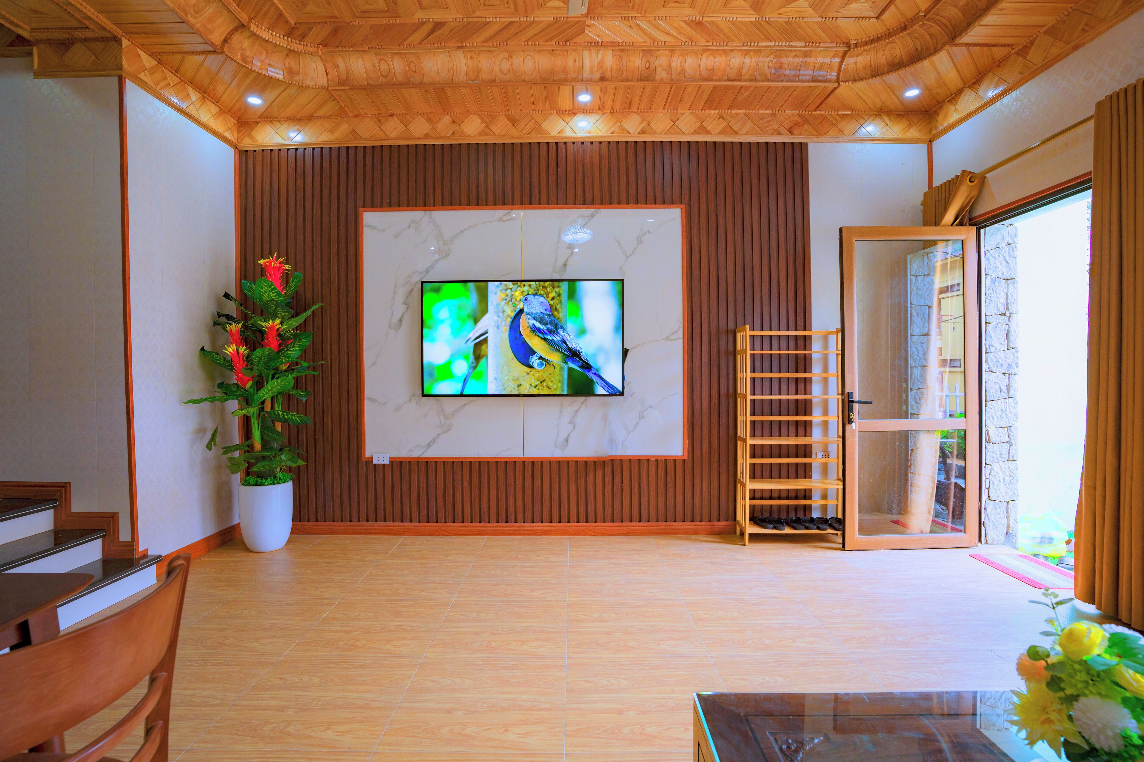 A hotel lobby with a wooden ceiling, a large TV on the wall, a potted plant, and a shoe rack.