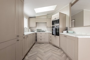 A modern kitchen with light wood cabinets, a herringbone floor, a skylight, and stainless steel appliances.