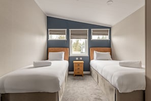 A twin room with two beds, a small wooden nightstand, and a window with blinds.