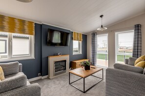Un salon moderne doté d’une cheminée, d’un téléviseur à écran plat et d’une grande fenêtre avec des rideaux.