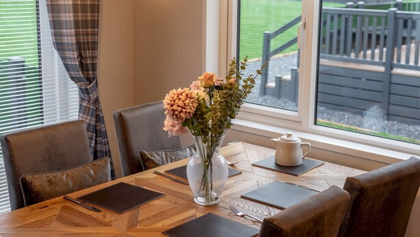A dining table with a vase of flowers, a teapot, and a laptop.
