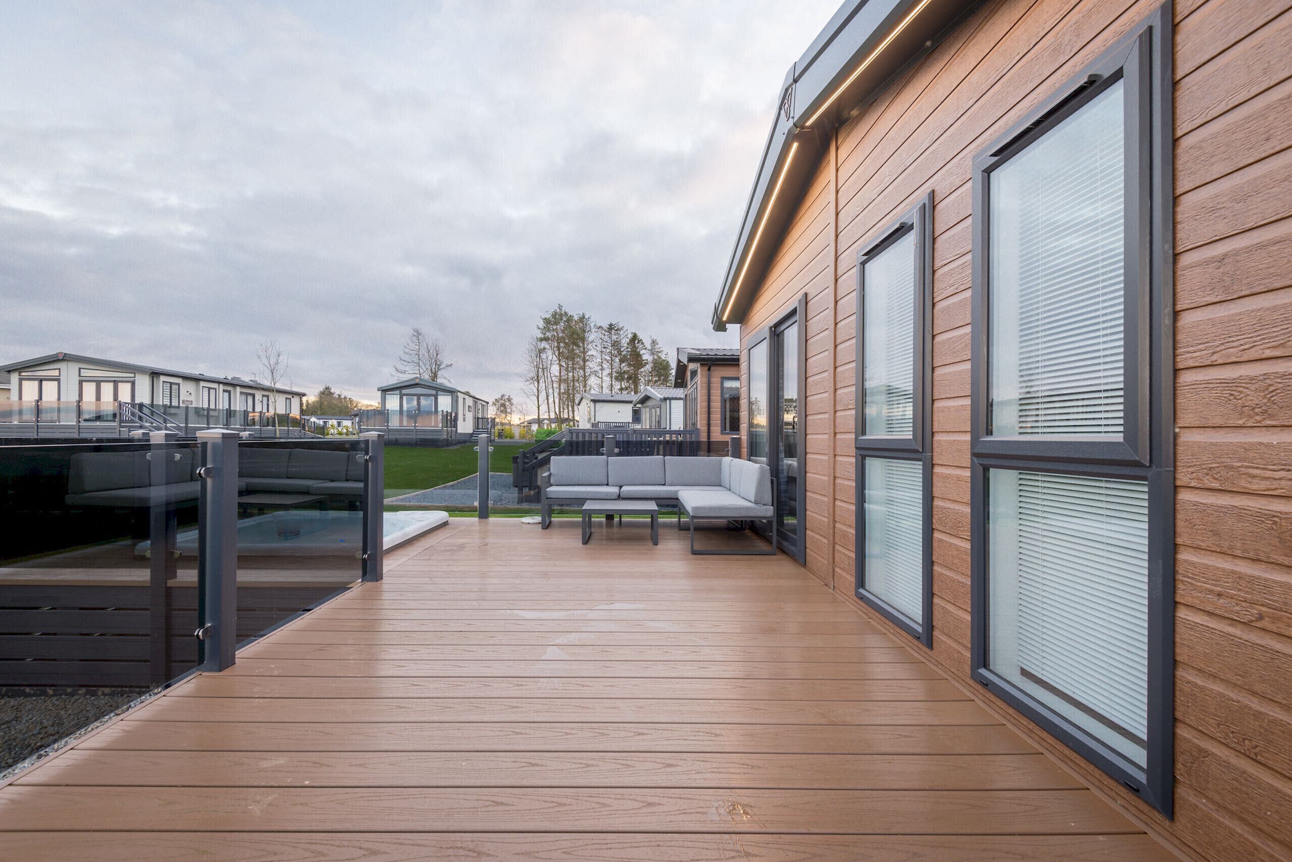 Eine moderne Außenterrasse mit Holzboden, einer grauen Couch und einem Glasgeländer.