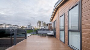 A modern outdoor deck with a wooden floor, a gray sofa, and a glass railing.