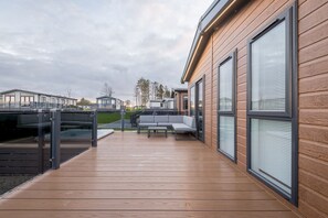 A modern outdoor deck with a wooden floor, a gray sofa, and a glass railing.