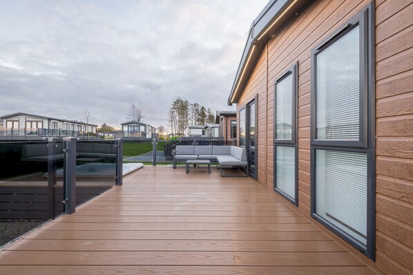 A modern outdoor deck with a wooden floor, a gray sofa, and a glass railing.
