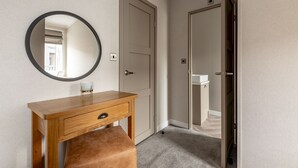 A room with a wooden desk, a round mirror, and a bench. There are two doors, one leading to a bathroom and another to a closet.