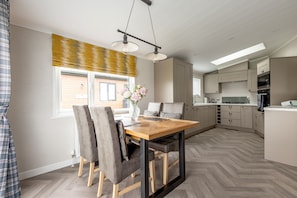 A modern kitchen with a central island, built-in appliances, and a dining area with a wooden table and chairs.