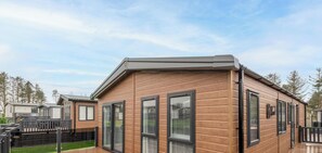 A modern short stay building with a wooden exterior, large windows, and a deck area. - Lodge No 85 | Hot Tub | Stewart's Resort Cameron (Cameron)
