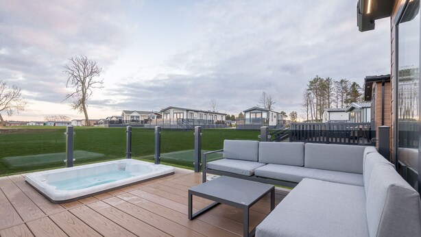 Eine Terrasse mit Whirlpool, einer grauen Couch und einem kleinen Tisch.