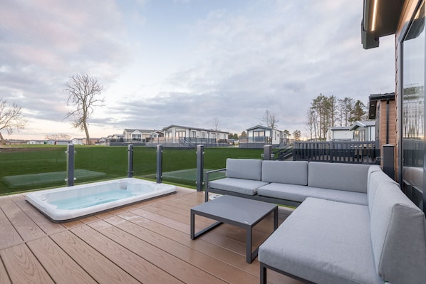 A deck with a hot tub, a gray sofa, and a small table.