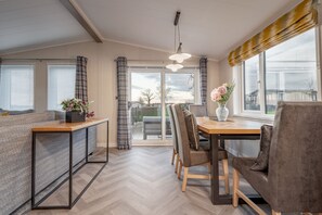 A modern kitchen with a wooden table and chairs, a herringbone-patterned floor, and large windows with curtains.