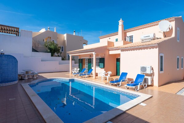 A swimming pool with lounge chairs, a covered seating area, and a building with a satellite dish.