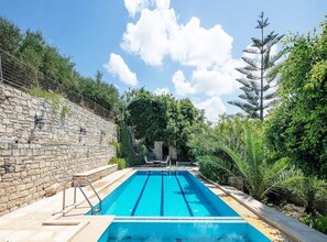 A rectangular swimming pool with clear blue water, surrounded by stone walls and lush greenery. - Villa Anta With 2 Bedrooms and 1 Bathrooms (Rethymno)