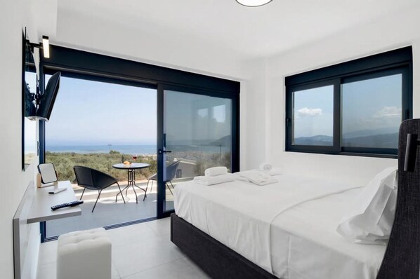 Une chambre moderne avec un grand lit, un bureau avec une chaise et un balcon équipé d’une table et de chaises.
