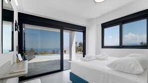 A modern bedroom with a large bed, a desk, and a view of the ocean through a sliding glass door. - Villa Andria With 5 Bedrooms and 5 Bathrooms (Lefkada)