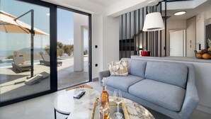 A modern living room with a sofa, a glass door leading to an outdoor area, and a dining table with a bottle and glass. - Villa Andria With 5 Bedrooms and 5 Bathrooms (Lefkada)