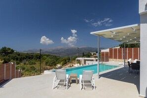 A pool area with two lounge chairs and a table, a covered patio, and a view of mountains. - Casa di Pietra With 2 Bedrooms and 3 Bathrooms (Kefalonia)