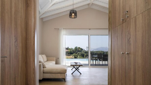 Un salon moderne avec un canapé, une petite table et une vue sur un balcon aménagé avec du mobilier d’extérieur.