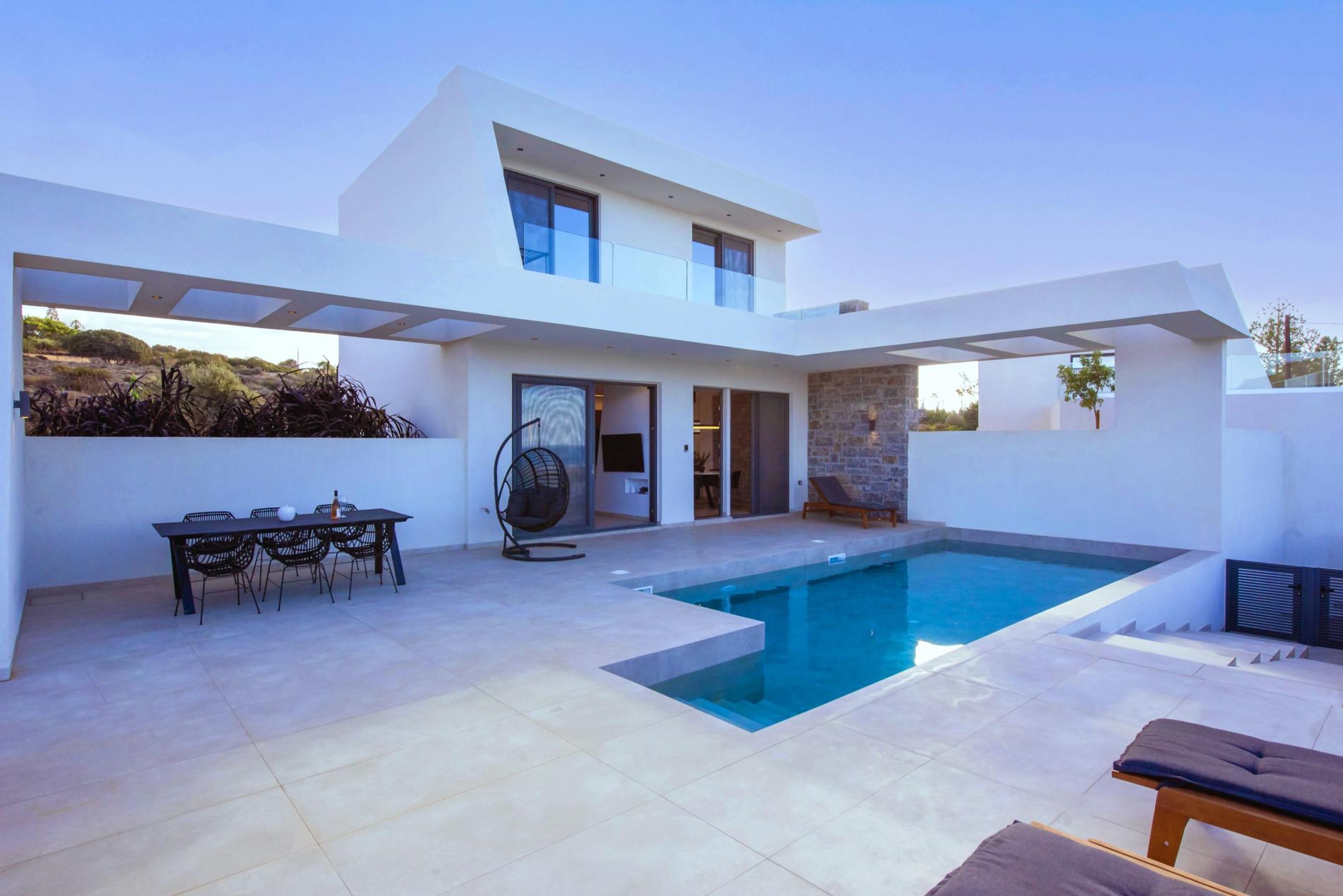 Una casa moderna con piscina, zona de comedor con mobiliario exterior y una pared de piedra.
