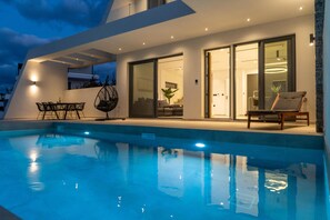 A modern outdoor pool area with a glass-enclosed patio, a lounge chair, and a dining set. - Aethra Deluxe Villa With Pool 700m From Beach (Hersonissos)