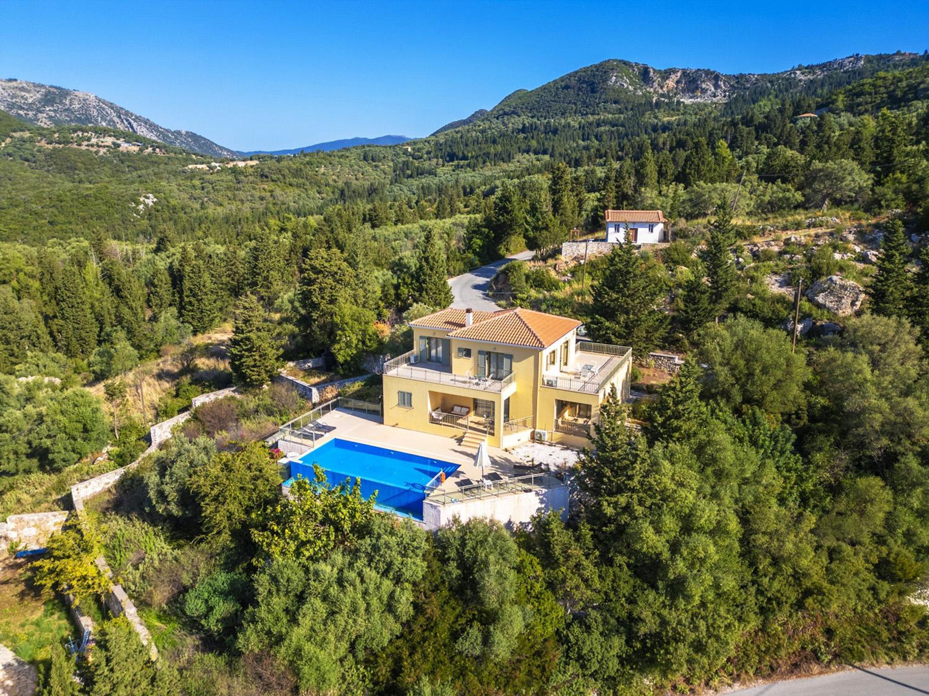 A two-story house with a swimming pool, surrounded by dense forest and mountains.