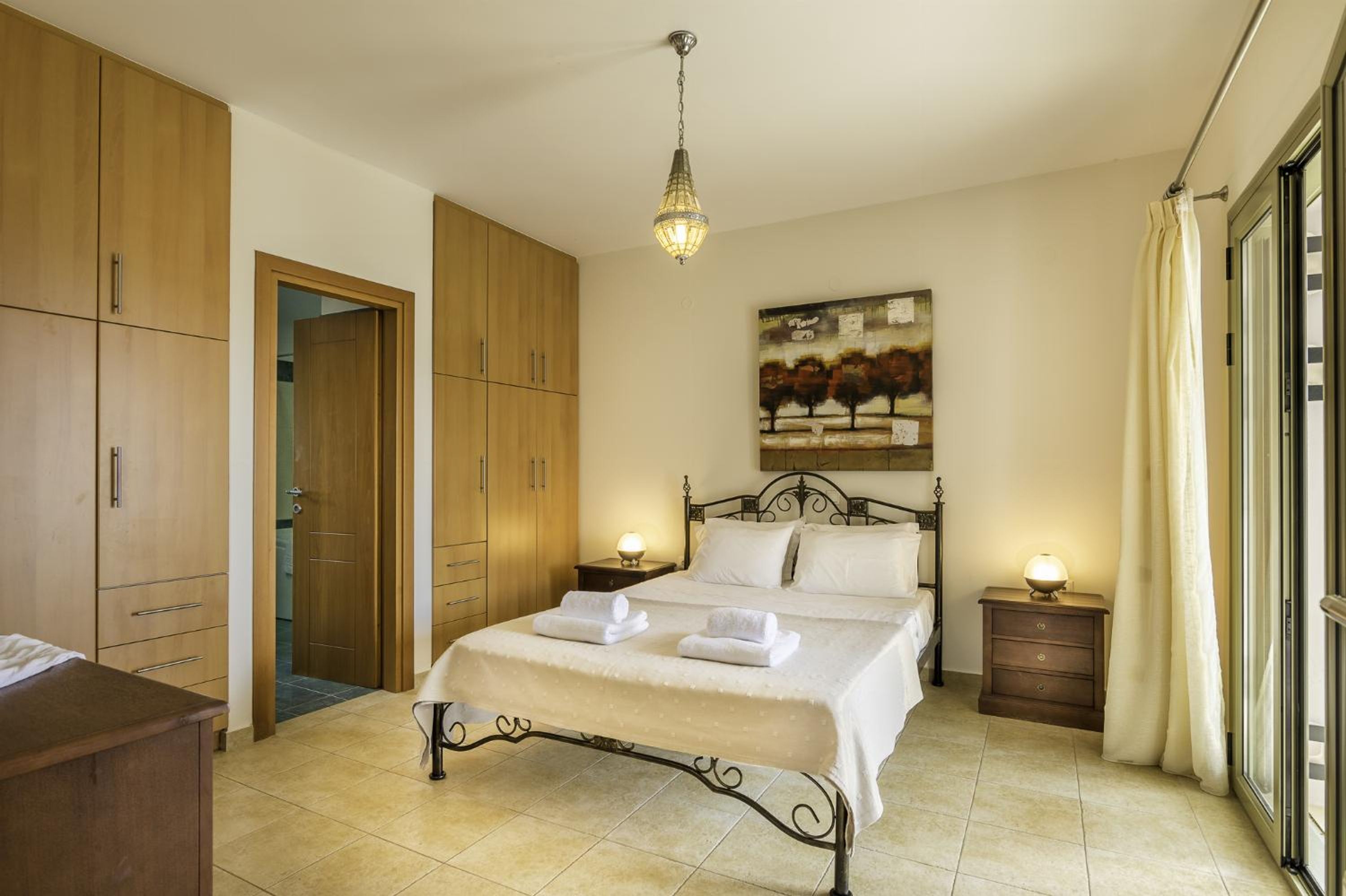 A bedroom with a bed, wooden wardrobe, a painting, and a nightstand.