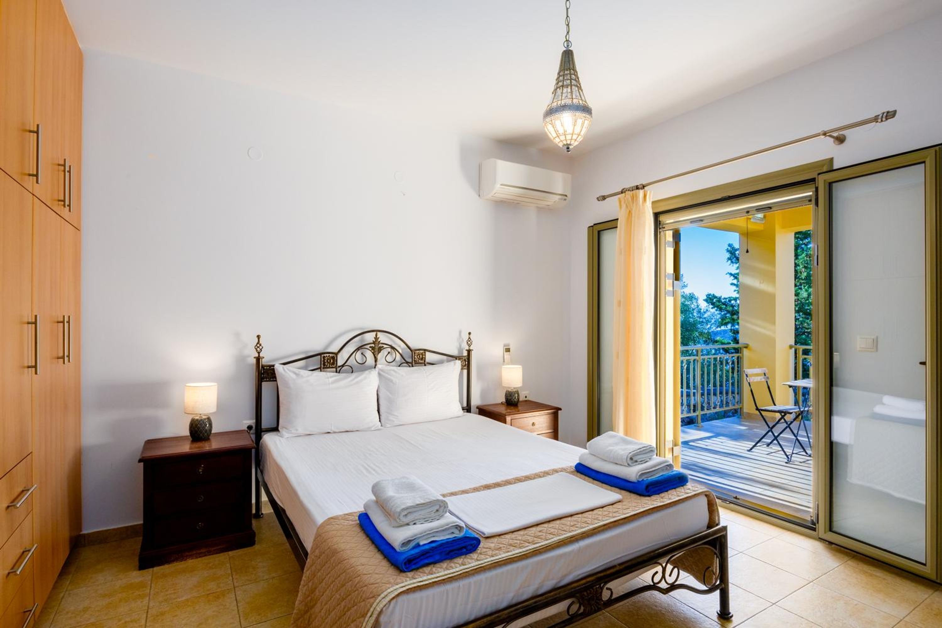 Une chambre à coucher comprenant un lit, des tables de chevet, une armoire, un appareil de climatisation et un balcon avec vue.