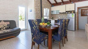 Ein Essbereich mit einem Holztisch und blau gepolsterten Stühlen, einer Obstschale und einer Küche im Hintergrund.