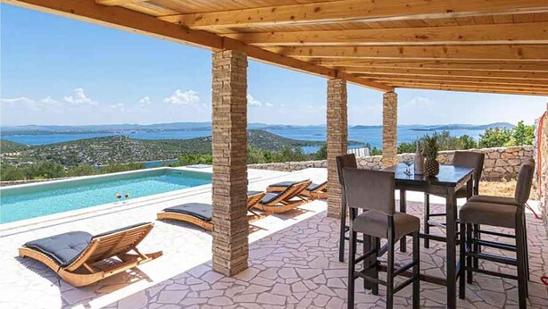 Ein überdachter Außenbereich mit Pool, Liegestühlen und einem Tisch mit Stühlen.