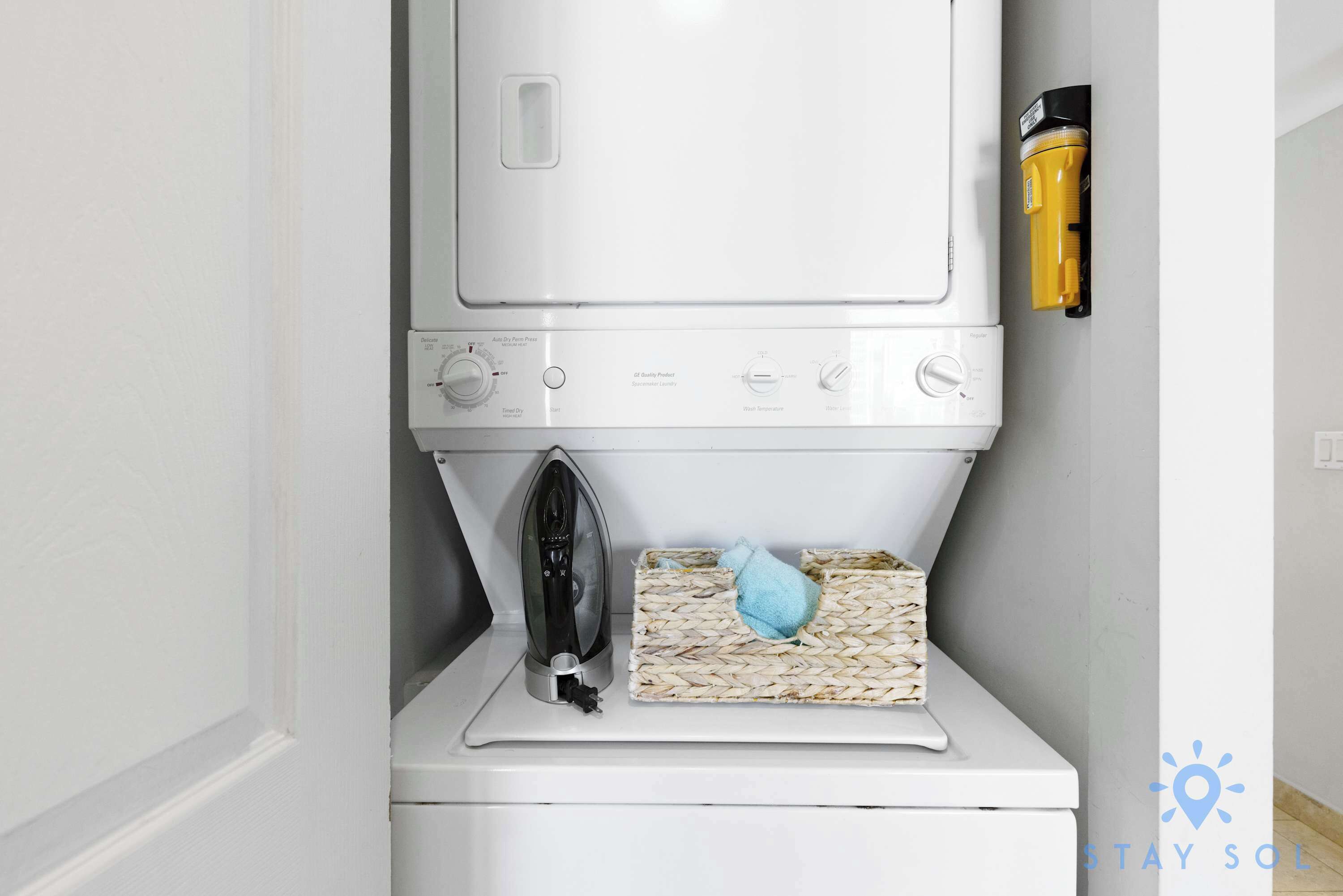 A compact washer and dryer unit with a small iron and a woven laundry basket.