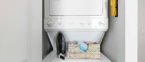 A compact washer and dryer unit with a small iron and a woven laundry basket.