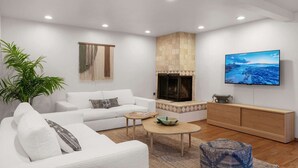 A modern living room with a white sofa, a coffee table, a TV mounted on the wall, and a fireplace. - The OB Hideaway, pool, hot tub (San Diego)